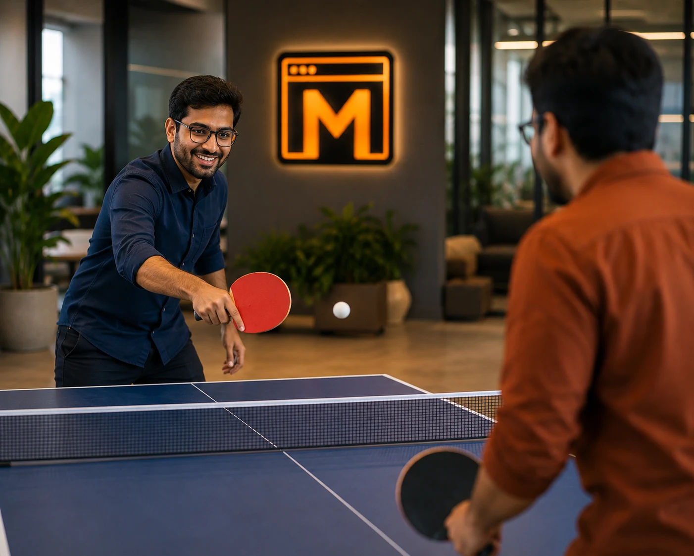 Two Mejona colleagues playing table tennis in the office lounge, paddles mid-swing, with the Mejona M logo softly lit on the back wall.